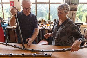  Jörg Otto erklärt Autorin Ulrike Hensel die Herausforderungen eines geschweiften und gelochten Obergurtes für die Rekonstruktion eines historischen Zauns: Die Lochungen werden einzeln in streng definiertem Winkel gefertigt werden, damit die Füllstäbe genau senkrecht verlaufen. 