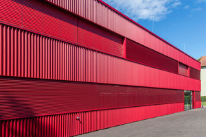  Die Fassade, bestehend aus roten Metalllamellen, fasst alle Baukörper zu einem Ensemble zusammen.  