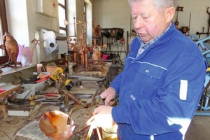  Der Wetterfahnenmacher erhitzt an seiner Werkbank das Kupferblech, um es mit dem Treibhammer zu formen.  