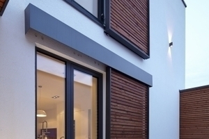 Sonnenschutzelemente mit Holzfüllungen bilden an drei Fassadenseiten einen Kontrast zur hellen Grundfarbe.  